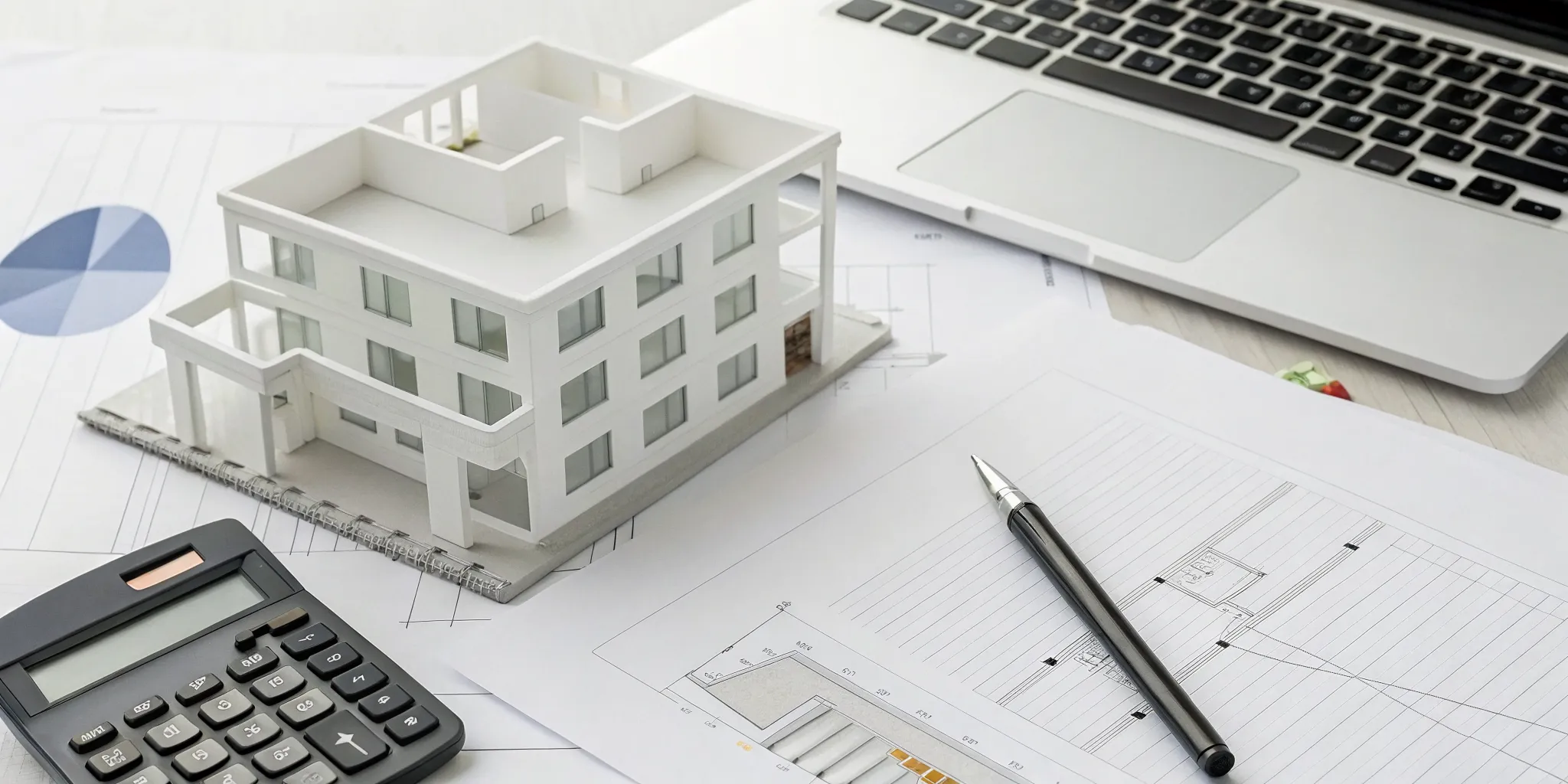 Real estate business tax planning with a house model, calculator, and laptop on a desk.